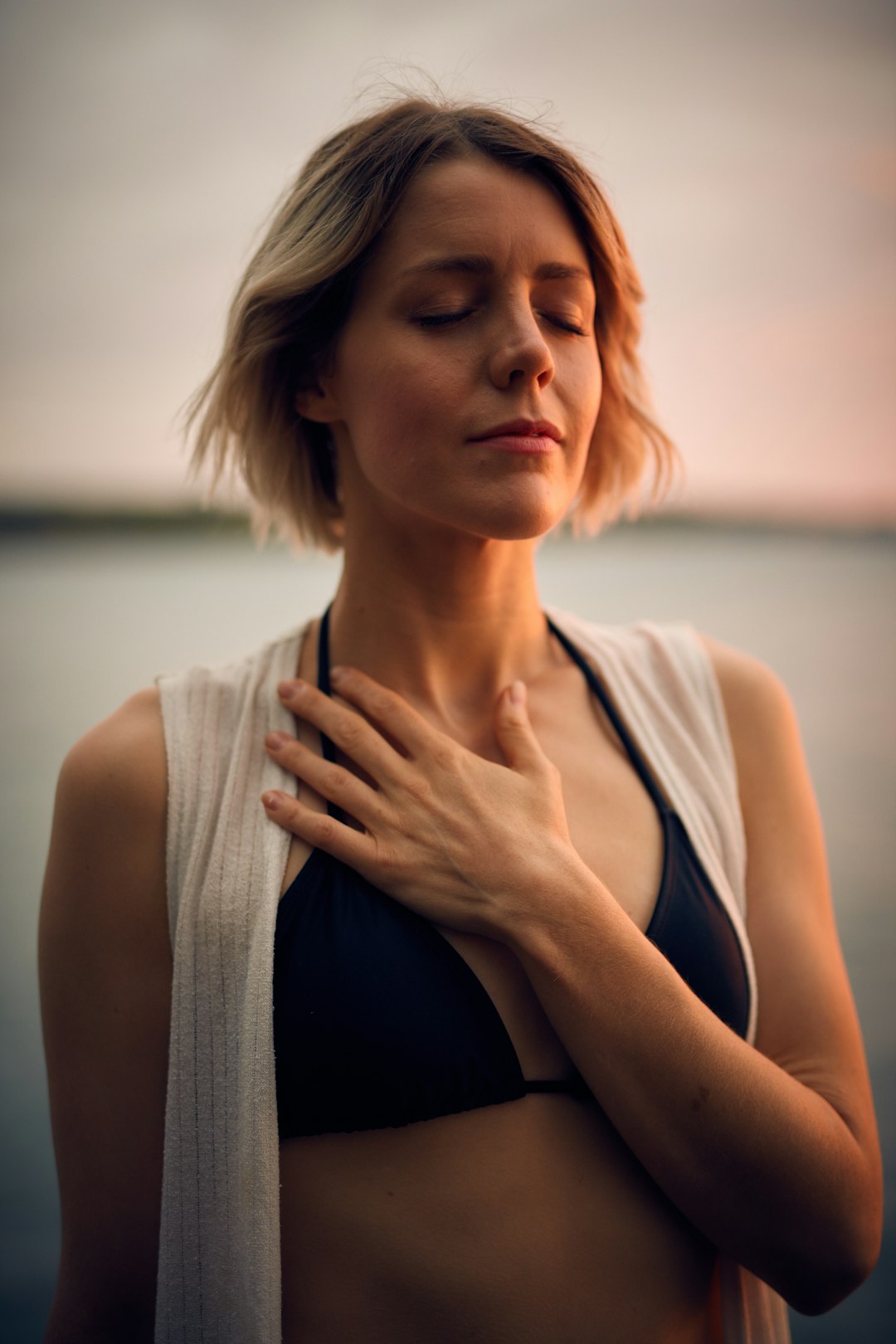Feel deeper. Think higher by Athletic Brands woman in white vest and black bikini with hand on chest